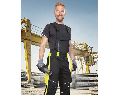 Bărbat în haine de lucru cu salopetă, mănuși de lucru și țeavă pe fundal industrial