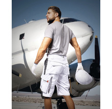 Bărbat cu pantaloni scurți de lucru cu mai multe buzunare în fața unui avion