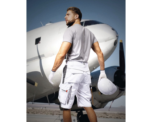 Bărbat cu pantaloni scurți de lucru cu mai multe buzunare în fața unui avion