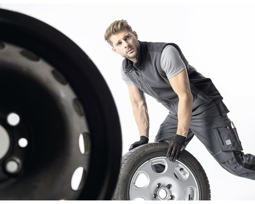 Un bărbat în haine de lucru manipulează o anvelopă și o jantă.