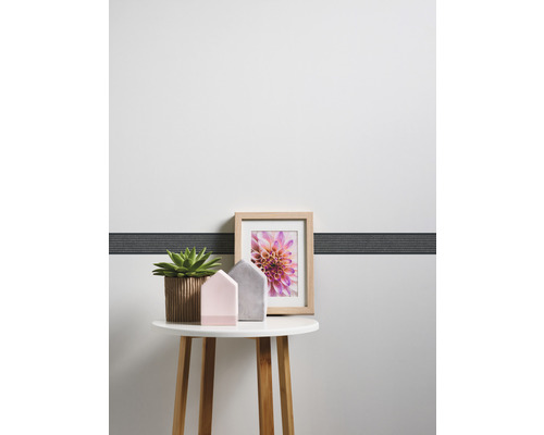 Măsuță decorativă cu plantă de interior, case decorative și ramă foto în fața unui perete cu bordură