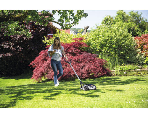 Femeie care operează o mașină de tuns iarba pe un gazon într-o grădină.