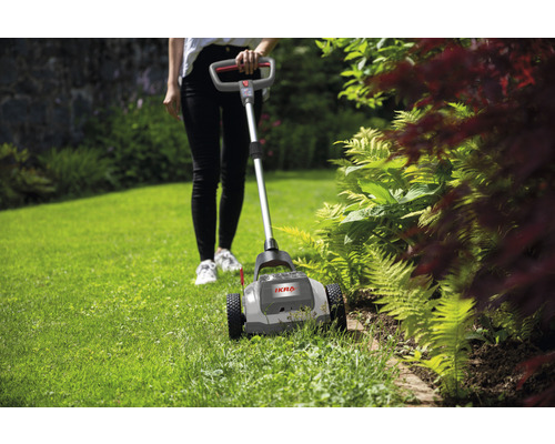 Grădinăreasă care lucrează cu un tăietor de margini de gazon în grădină.