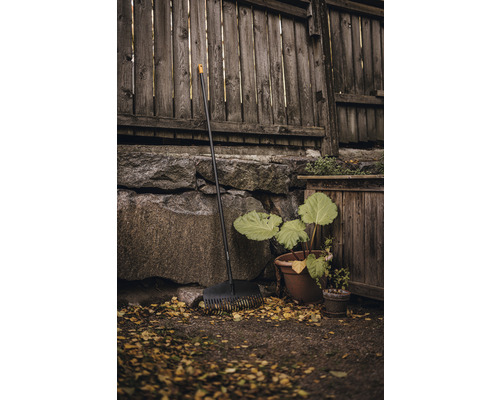 Greblă de frunze din plastic în fața gardului de lemn și a zidului de piatră