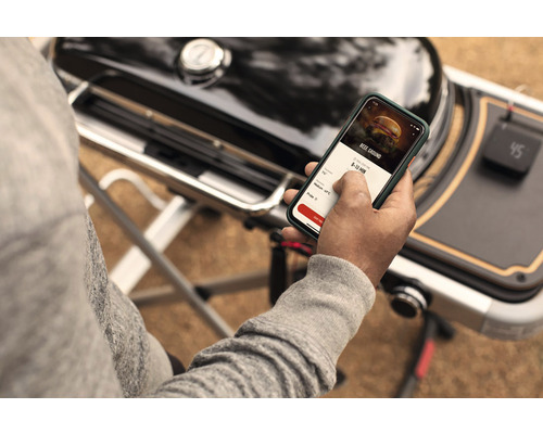 O persoană folosește o aplicație pe un smartphone lângă un grătar.