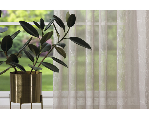 Șaluri decorative cu model de frunze lângă o plantă de interior în ghiveci în fața unei ferestre