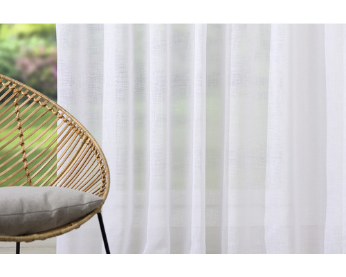 Scenă cu un scaun din ratan cu pernă și o perdea albă.