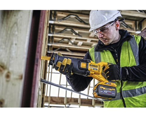 Un muncitor în construcții folosește un fierăstrău sabie cu acumulator DeWalt pe un șantier.