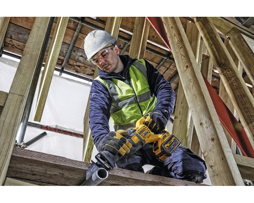 Un muncitor în construcții, purtând cască de protecție și ochelari de protecție, taie o țeavă cu un ferăstrău electric DeWalt.
