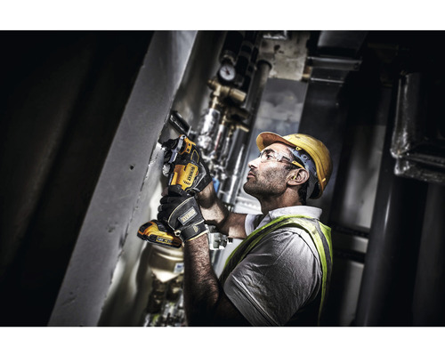 Un meșter în echipament de protecție folosește o unealtă electrică oscilantă DeWalt pe un perete.