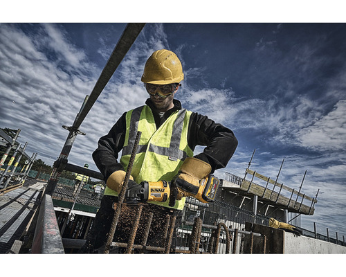Muncitor în construcții cu cască de protecție și vestă de protecție care lucrează cu un polizor unghiular pentru a tăia bare de armare pe un șantier