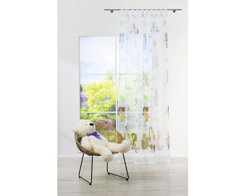 Fulare decorative cu motive animale în fața unei ferestre, în cameră se află un fotoliu cu un ursuleț de pluș