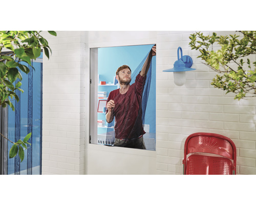 Un bărbat fixează o plasă de țânțari pe o fereastră în aer liber.