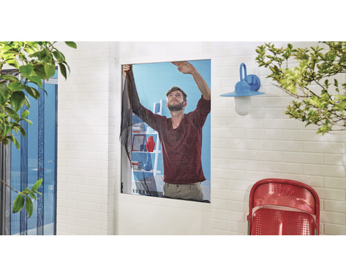 Un bărbat fixează o plasă de insecte pe o fereastră într-o cameră luminoasă