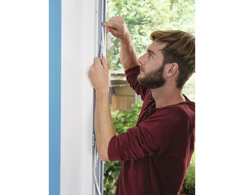 Un bărbat fixează bandă de etanșare pe un cadru de fereastră.
