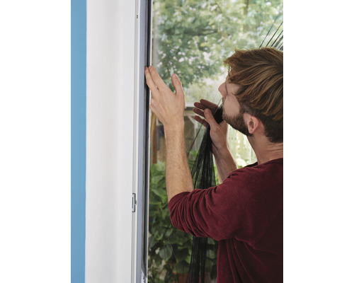 Bărbat care fixează o plasă de insecte pe un toc de fereastră.