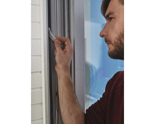 Un bărbat instalează o plasă de țânțari la fereastră