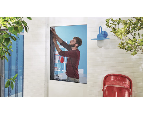 Bărbat care instalează plasă de insecte la fereastra unei case cu un perete de cărămidă și iluminat exterior