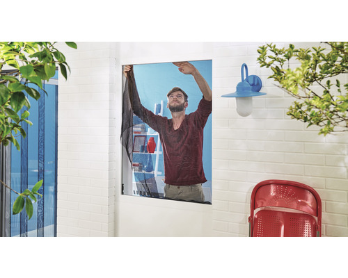 Un bărbat montează o plasă de țânțari la o fereastră pentru a împiedica intrarea insectelor.