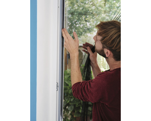 Un bărbat atașează o plasă de țânțari de cadrul ferestrei ca protecție împotriva insectelor.