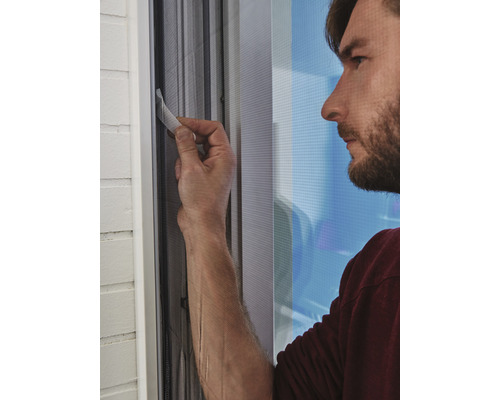 Un bărbat fixează o plasă de insecte pe un cadru de fereastră