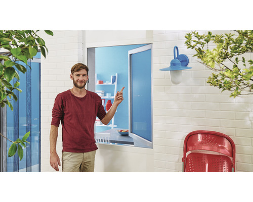 Un bărbat stă în fața unei ferestre cu plasă de insecte și arată spre ea.