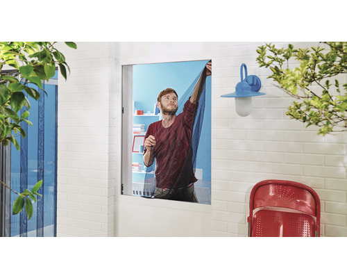 Un bărbat montează o plasă de protecție împotriva insectelor în fața unei ferestre.