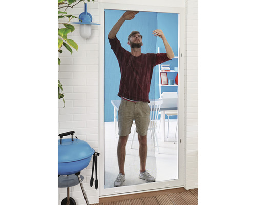 Bărbat montează plasă de insecte la o ușă de terasă. În fundal se pot vedea un grătar și mobilier de grădină.