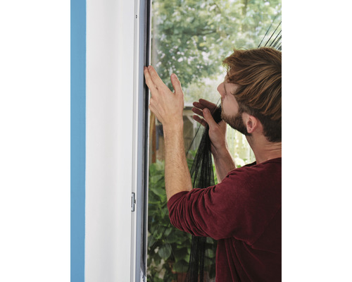 Un bărbat fixează o plasă de insecte pe un cadru de fereastră.