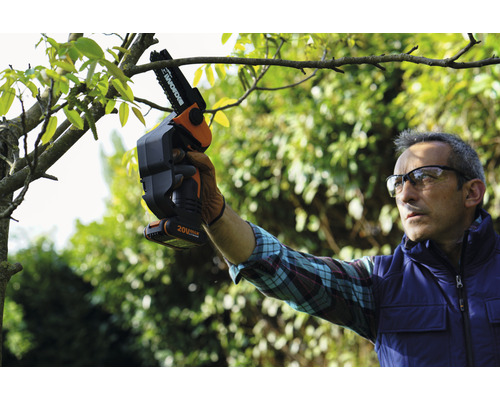 O persoană folosește un ferăstrău electric cu acumulator pentru a tăia un copac.