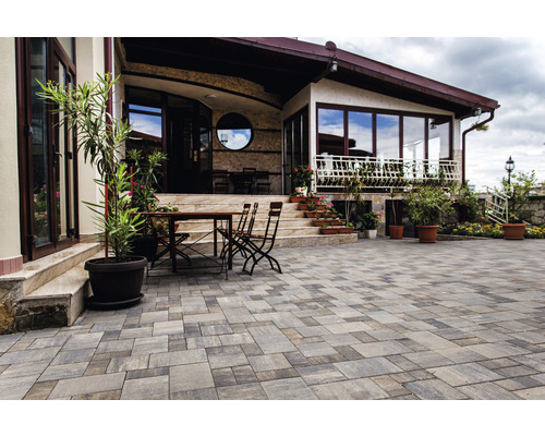 Terasă cu pavaj, masă și scaune în fața unei case