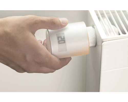 O mână reglează un termostat inteligent de radiator pe un radiator