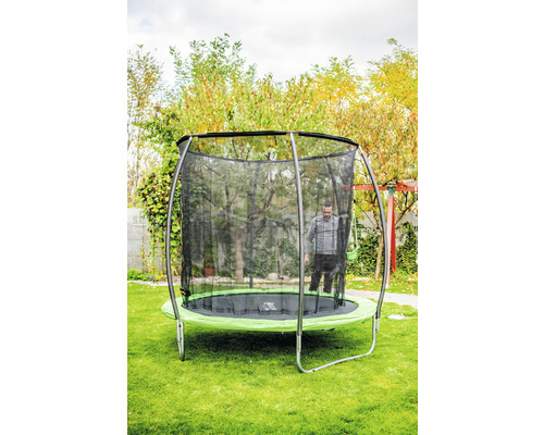 Scenă de grădină cu o trambulină rotundă cu plasă de siguranță și o persoană în interior