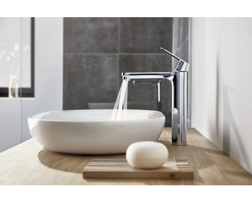 Pe o masă de lemn se află o chiuvetă ceramică și un robinet metalic cu apă curgătoare într-o baie.