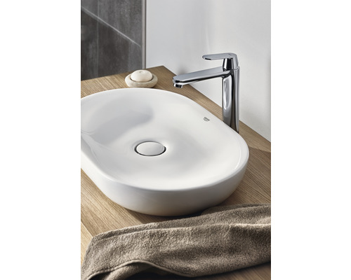 Chiuvetă ceramică pe blat cu robinet și prosop pe o suprafață din lemn.