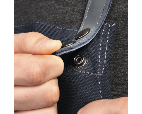 Prim-plan cu o persoană care fixează o capsă pe un șorț de lucru albastru.