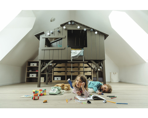 Cameră de joacă pentru copii cu pat tip căsuță în copac, rafturi și copii jucându-se pe podea