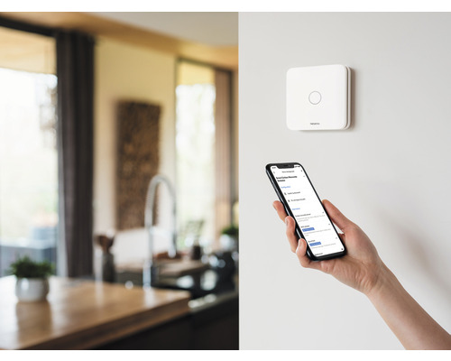 Senzor inteligent de suprafață Netatmo și smartphone într-o cameră modernă.