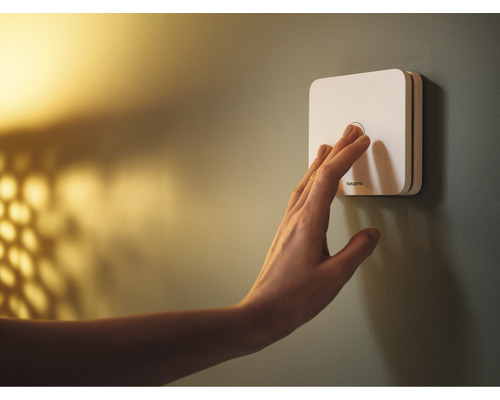 Mână acționând comutatorul Netatmo de pe perete