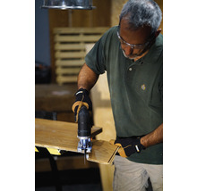 Un bărbat folosește un fierăstrău vertical pentru a tăia o bucată de lemn. Poartă ochelari de protecție și mănuși.