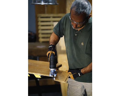 Un bărbat folosește un fierăstrău vertical pentru a tăia o bucată de lemn. Poartă ochelari de protecție și mănuși.