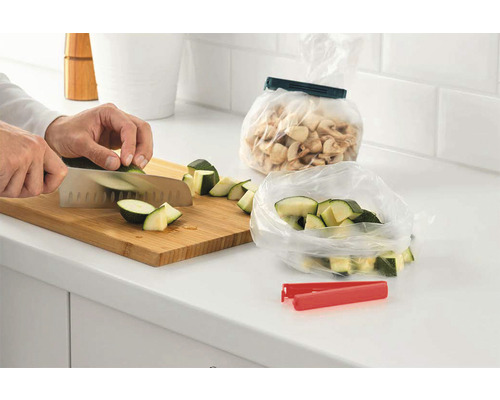 O persoană taie dovlecei pe un tocător lângă o pungă resigilabilă pe un blat de bucătărie.