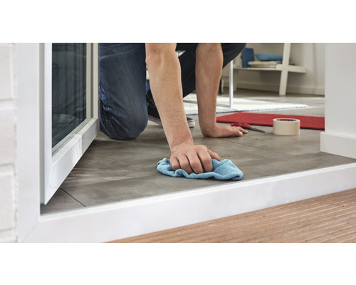 O persoană șterge podeaua cu o cârpă lângă o fereastră.