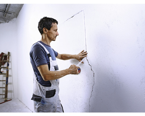 Un bărbat izolează un perete cu bandă de mascare.