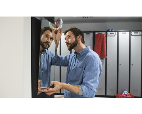 Bărbat care fixează o oglindă cu bandă adezivă dublă într-un vestiar.