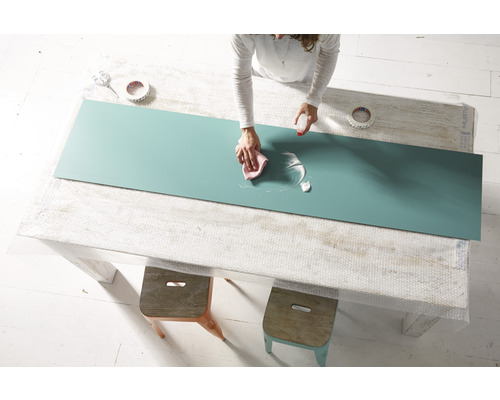 Femeie curăță un blat cu detergent și o cârpă pe o masă.