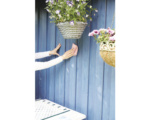 Curățarea unui perete de grădină din lemn cu o cârpă, cu coșuri suspendate cu flori.