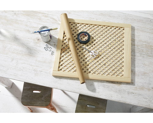 Cadru din grilaj de lemn cu materiale de pictură, bandă adezivă și foarfece pe o masă.