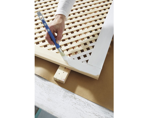 O persoană vopsește un spalier de lemn cu o pensulă.