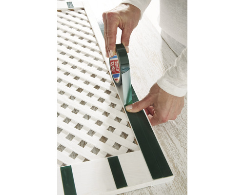 O persoană aplică bandă adezivă Tesa pe un grătar alb.